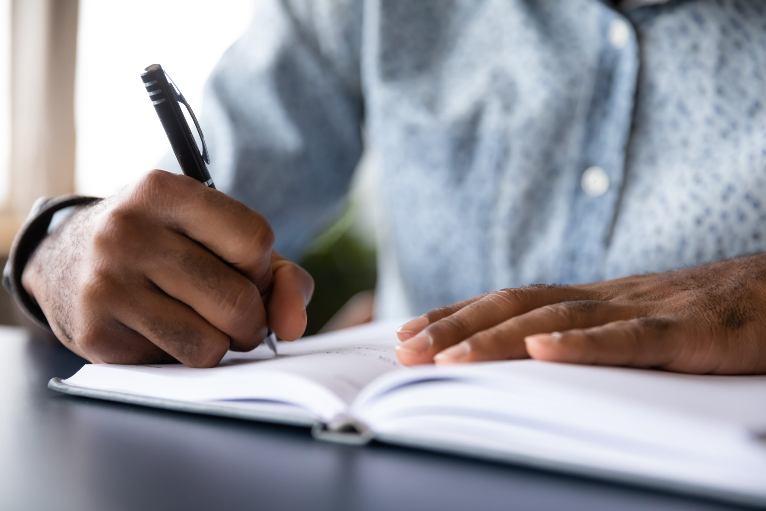 Hands holding a pen while writing in a notebook