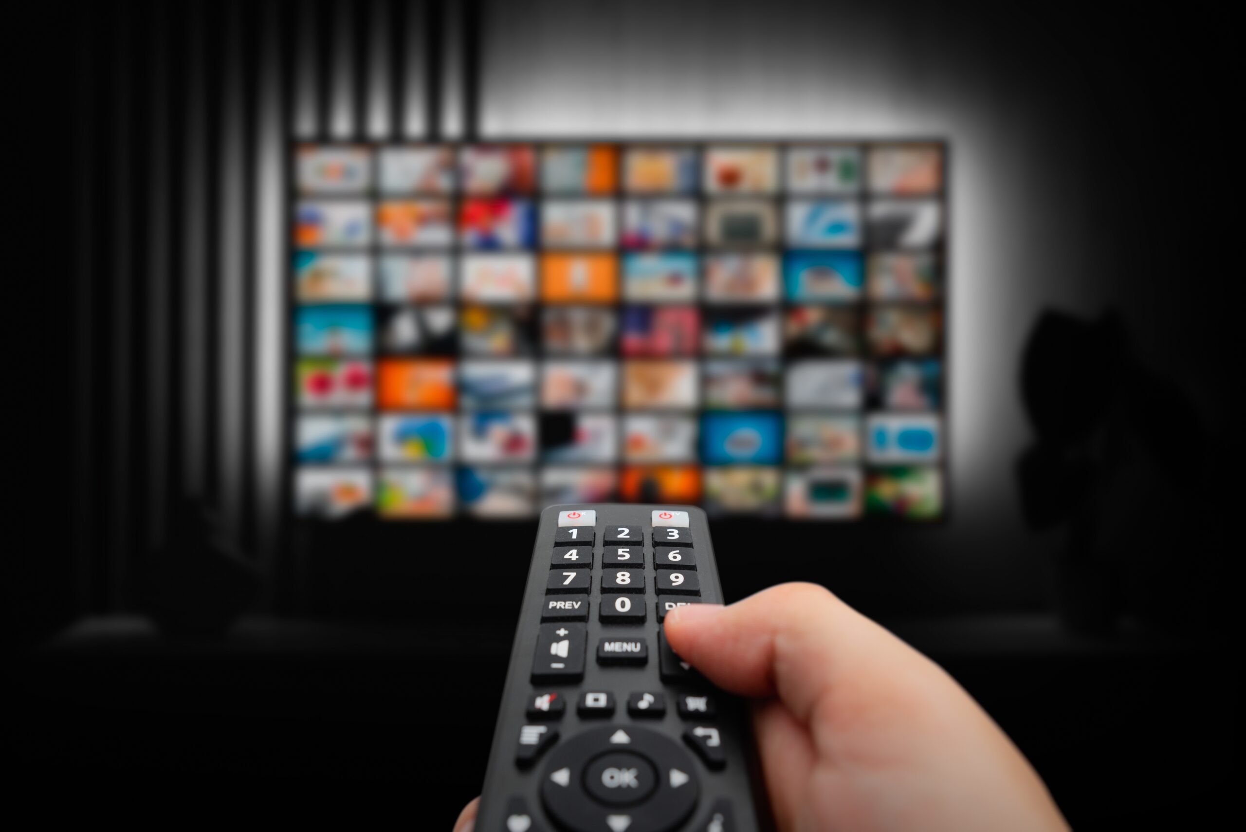 A hand pointing a remote at a TV with lots of streaming options on screen