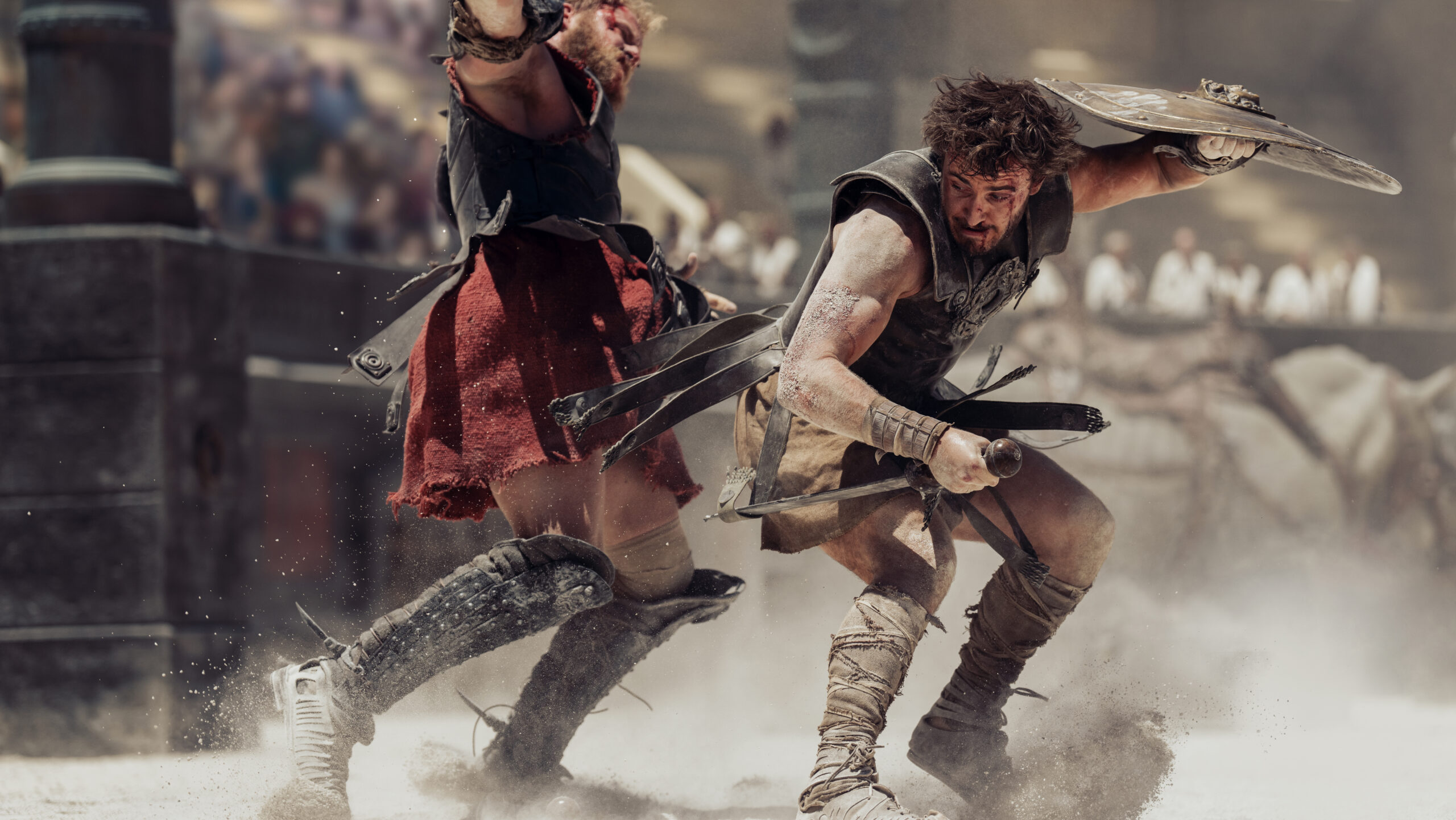 Two gladiators fighting in a sandy arena while the crowd watches on
